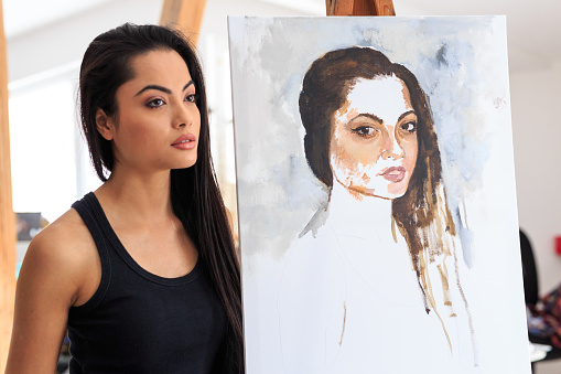 Female model posing next to her portrait in workshop.