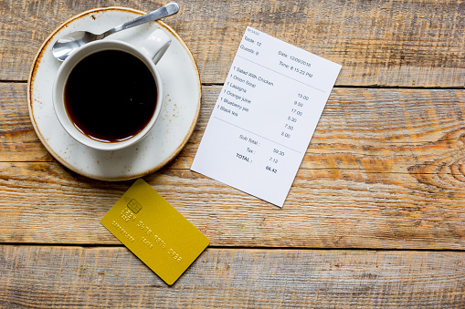 credit card for paying, cup of coffee and check on cafe wooden desk background top view mock up