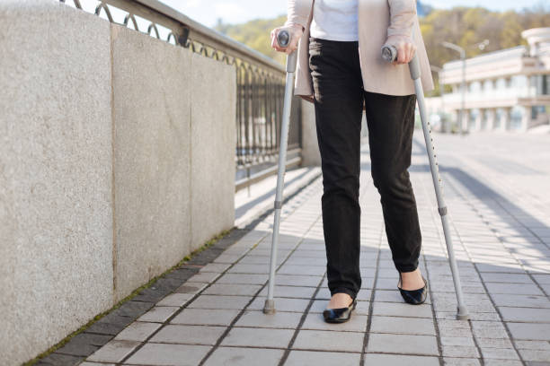 Not fun getting on. Moody shy thoughtful lady using crutches and concentrating while walking outdoors
