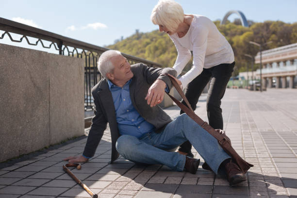Merry pensioner sitting on the street and receiving help Genuine desire to help others. Old cheerful lovely man tripping over and spanking down while delicate woman raising this man t cell photos stock pictures, royalty-free photos & images