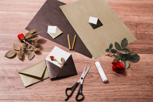 istock Color paper. Small colored envelopes. Making a greeting card. Workplace designer. Romantic letter. Flower arrangement with stationery items. Red roses with green leaves on wooden background. Flat lay 684548802