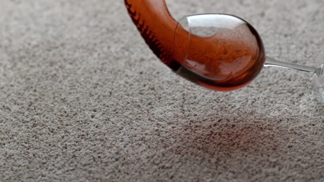 Glass of red wine spilling on carpet in slow motion