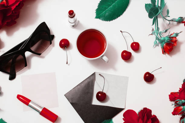 frame of red beautiful roses with green leaves, lady lipstick, red tea, black glasses, a ring with a black stone, envelope, ripe cherries and a leaf of paper lie on a white background. flat lay, art - flower cherry cup tea imagens e fotografias de stock