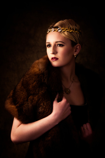 Vertical studio shot on mixed brown classic backdrop of 17 year old blonde model in fur stole and head band. Waist up, looking to viewer's left with chin in fur. Warm glow feel.