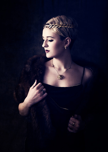 Vertical low key studio shot on mixed brown classic backdrop of 17 year old blonde model in fur stole and head band. Waist up, profile, touching fur. Cross processed to create Old Masters painting feel.