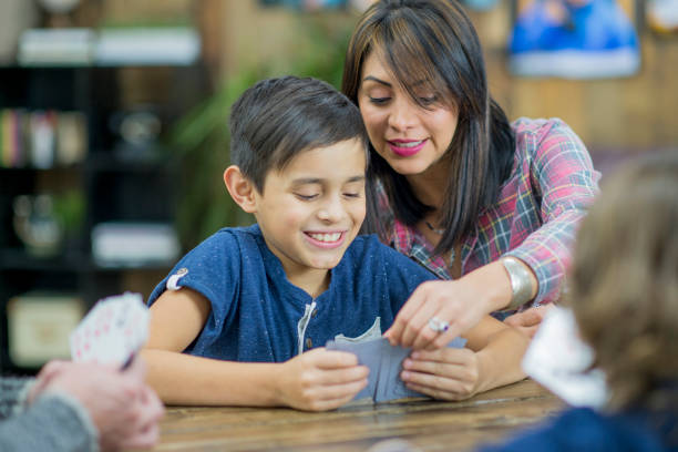 A young boy with a bright smile hands a blurred business card forward. He's seated outdoors against a backdrop of potted plants, adding a touch of nature to the scene.