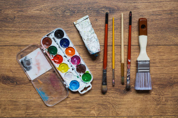 Artistic squirrel brushes, tubes of oil paints and watercolors on a wooden background.The palette of twenty-four colors .Used tools for artists and schoolchildren. Tools for art. Set of artistic tools cepillos artísticos de ardilla, tubos de pinturas al óleo y acuarelas sobre un fondo de madera. la paleta de veinticuatro colores. herramientas usadas para artistas y escolares. herramientas para el arte. conjunto de herramientas artísticas