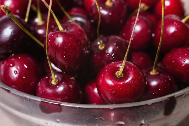 Ripe juicy red cherry with drops of water in a transparent plate on a wooden background.