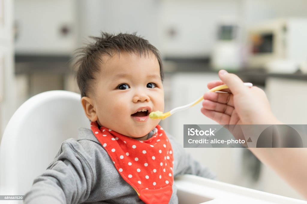 Petit garçon asiatique mangeant des aliments mélangés sur une chaise haute - Photo de Bébé libre de droits