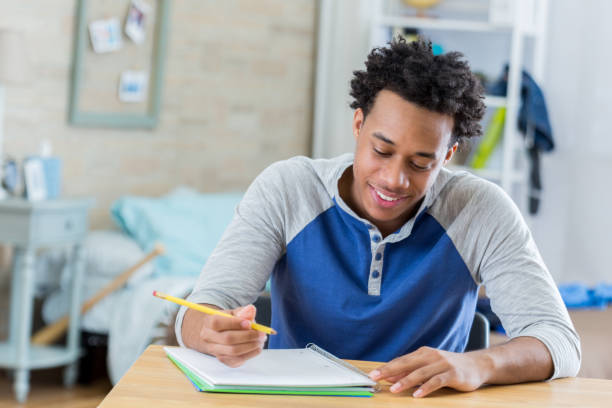 African American student works on homework Handsome African American teenage boy works on homework in his room. He is writing in a spiral notebook. dorm room photos stock pictures, royalty-free photos & images