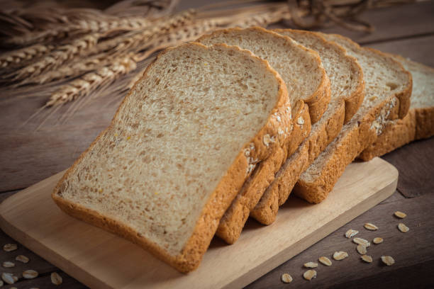 pan de trigo entero en la placa de madera - trigo integral fotografías e imágenes de stock