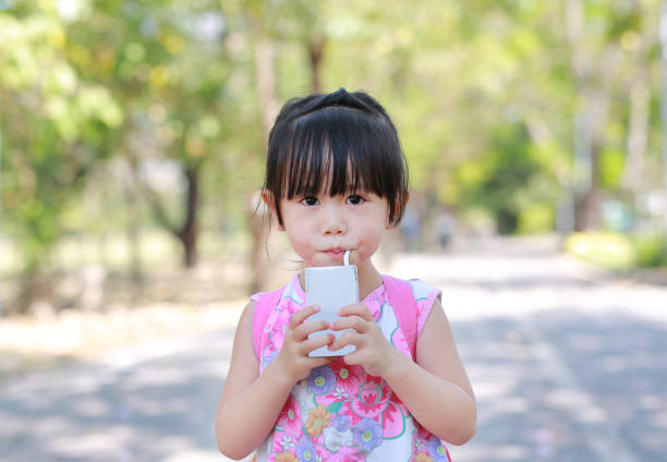 closeup of little girl drinking milk with straw in the park. portrait outdoor. - milk child drinking little girls imagens e fotografias de stock