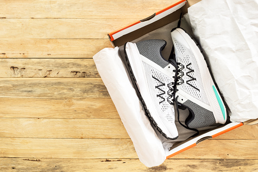 Pair of white sneakers in shoe cardboard box on wooden background\