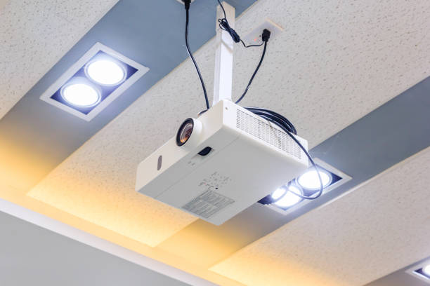 istock Multimedia projector hanging on the ceiling of modern conference room. Monochrome indoors picture 684735530