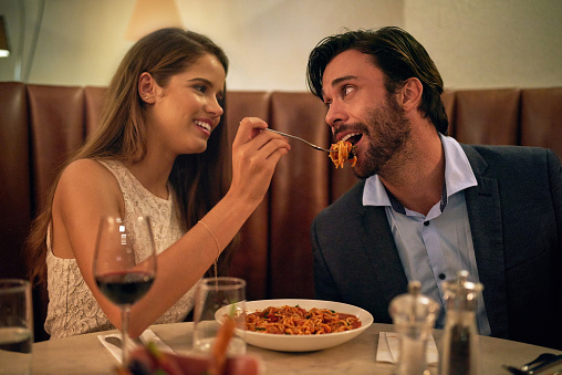 Shot of a young woman feeding her boyfriend a forkful of spaghetti during a romantic dinner date at a restaurant