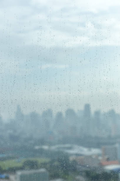 istock Rain drops on window glass and blurred cityscape and sunlight in background. 684774516