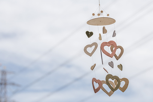 Heart shaped ceramic wind chimes hanging on window and defocused sky in background.