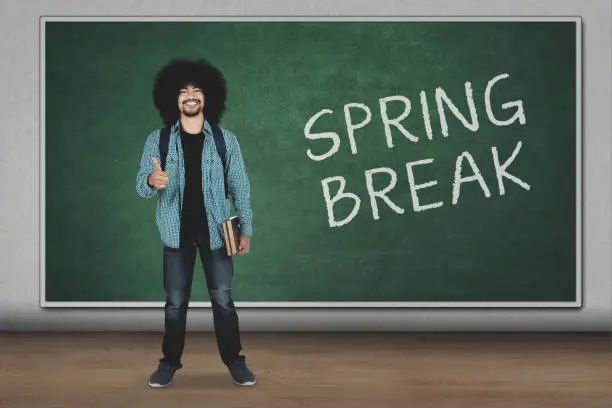 University student showing ok sign while standing with spring break word on chalkboard