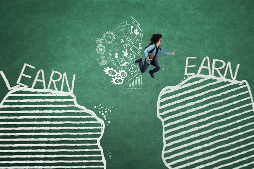 Young student jumping between gap with learn and earn words while holding a book