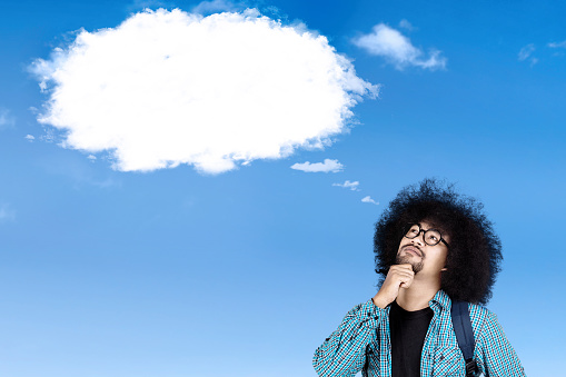 Afro college student thinking an idea while looking at empty cloud speech bubble on the sky