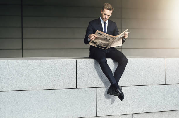 istock Stylish man with newspaper sits on brickwall 684806594