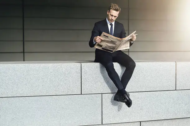 Cool businessman sits on a brick wall with newspaper