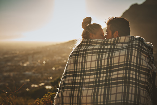 Shot of an affectionate couple wrapped in a blanket while spending time out in nature