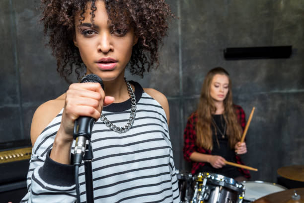Young singer standing with microphone while friend playing drums, hard rock music concept