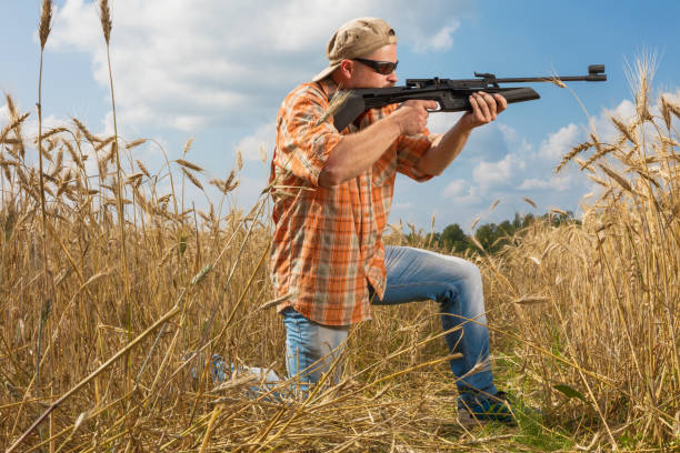 istock Hunter on cap and sunglasses aiming a gun at field 684873776