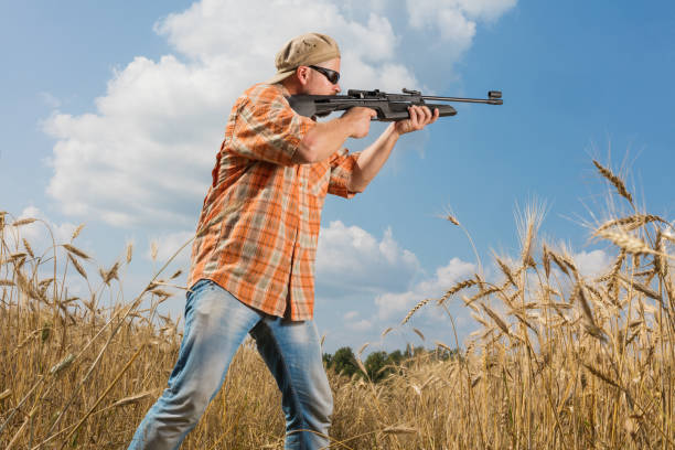 istock Hunter in cap and sunglasses aiming a gun at field 684873810