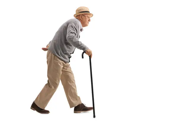 Full length profile shot of a senior walking with a cane isolated on white background