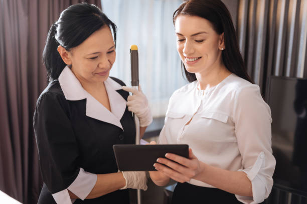 Joyful pleasant women looking at the tablet screen Pleasant communication. Joyful pleasant nice woman standing together and looking at the tablet screen while discussing work issues maid housework stock pictures, royalty-free photos & images