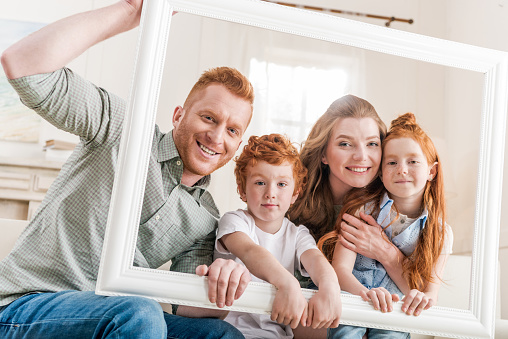 happy redhead family looking through white frame together, big family portrait concept