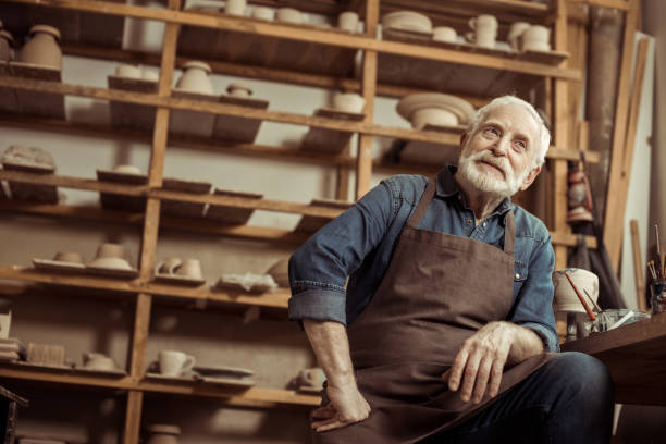 istock Senior potter in apron sitting at table and daydreaming at manufacturing 684968820