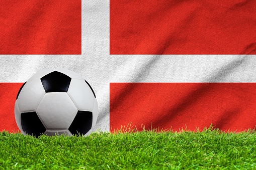 Football on grass field with wave flag of Denmark