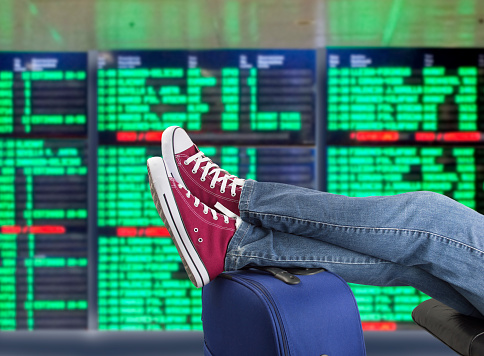 young man waiting for the plane at international airport with the flight information board