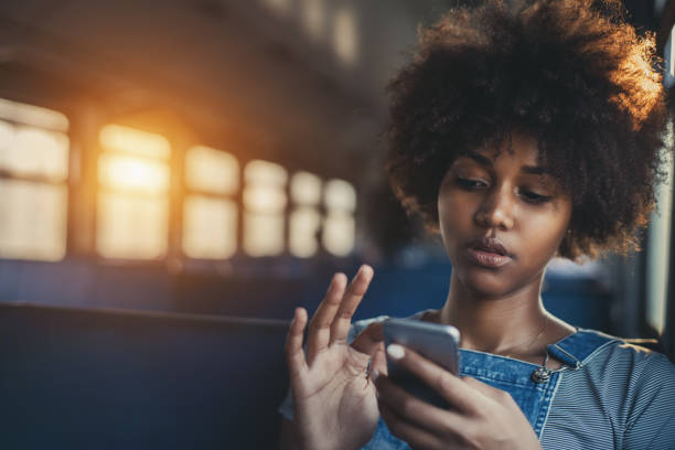 Cute mixed girl in train chatting via smartphone Thoughtful young biracial girl using smart phone while sitting alone in suburban train, curly african teenage female having online chat with her sister in train with copy space for your text or logo serious black teen stock pictures, royalty-free photos & images