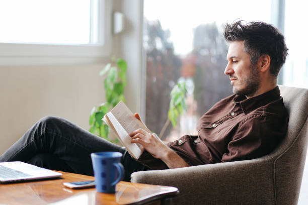 istock Young man reading a book at home 685047086