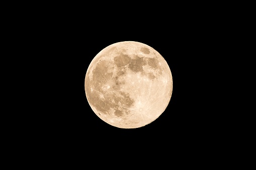 Horizontal photo of full moon. Moon with nice soft yellow color. Visible craters on the edge of space body. The bright and light areas on surface are clearly visible. Space around is black.