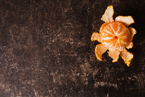 Ripe orange tangerine lies on a dark marble table with scratches. Juicy fruit. Flat lay