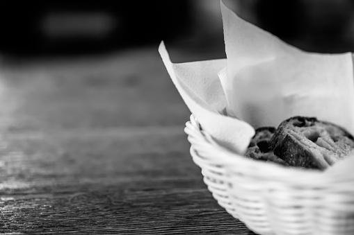 Slices of bread in the basket with blurred  wooden table background. Black and white.