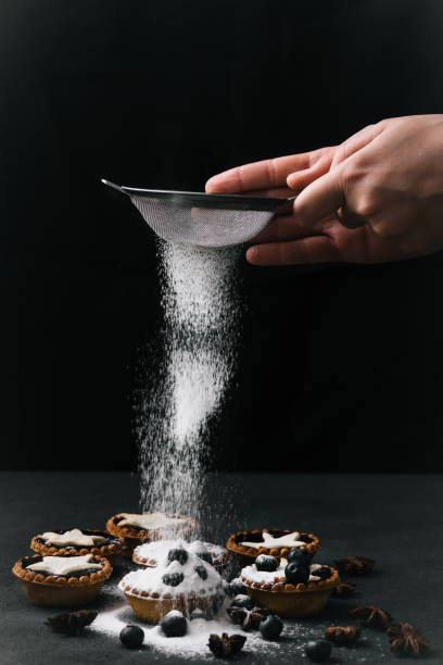 istock Hands scattering tarts with sugar powder, side view on black 685094552