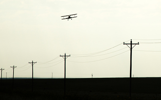 A small biplane flies over utility poles (silhouette)