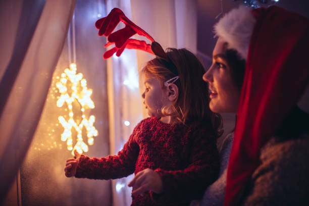 While waiting for Santa Claus Photo of a cute little girl with a Reindeer horns who is waiting for Santa Clause by the frosted window, along with her mother rudolph the red nosed reindeer photos stock pictures, royalty-free photos & images
