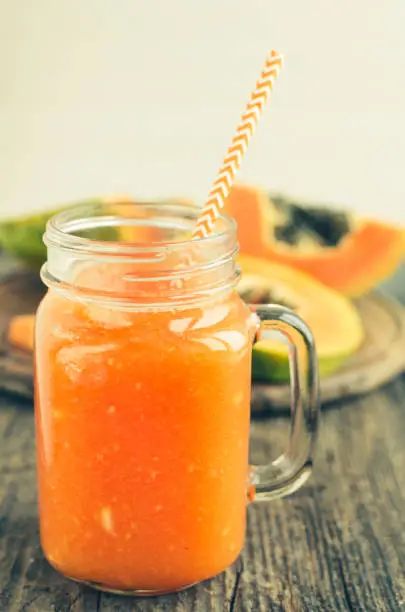 Papaya smoothie in glass mason jar on wooden table. Detox, diet, vegetarian food, healthy eating concept.
