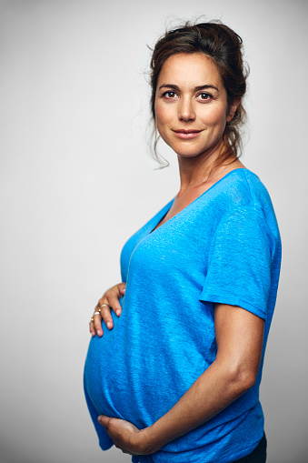 Side view of pregnant businesswoman with hands on stomach. Portrait of female professional is wearing casuals. Executive is standing over white background.