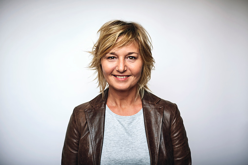 Portrait of mature businesswoman wearing leather jacket. Female is smiling. She is over white background.