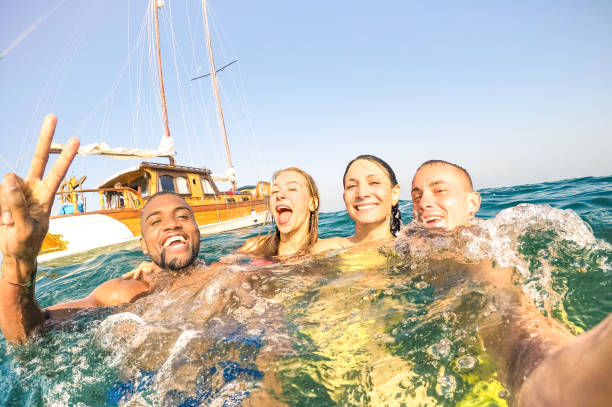 jeunes amis multiraciaux prenant le selfie et nageant sur le voyage en mer de bateau à voile - les garçons heureux riches et les filles ayant l’amusement dans le jour de partie d’été - concept exclusif de vacances - filtre chaud lumineux d’après - vacances photos photos et images de collection