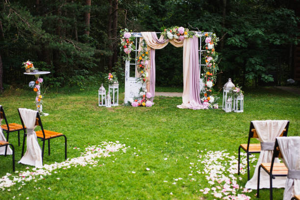 istock Beautiful wedding ceremony outdoors. Decorated chairs stand on the grass. Wedding arch made of cloth and white and pink flowers on a green natural background. Old doors, rustic style. 685146880