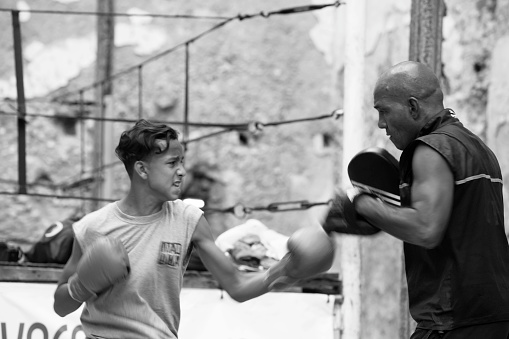 Young boxer training with his coach in front of the makeshift ring at Project Cuba Boxeo, an aid project from a non profit organisation Malaika Aid for Children. The organization brings boxing to Cuban children from 8-21 years of age. Old Havana, Cuba, black and white image.
